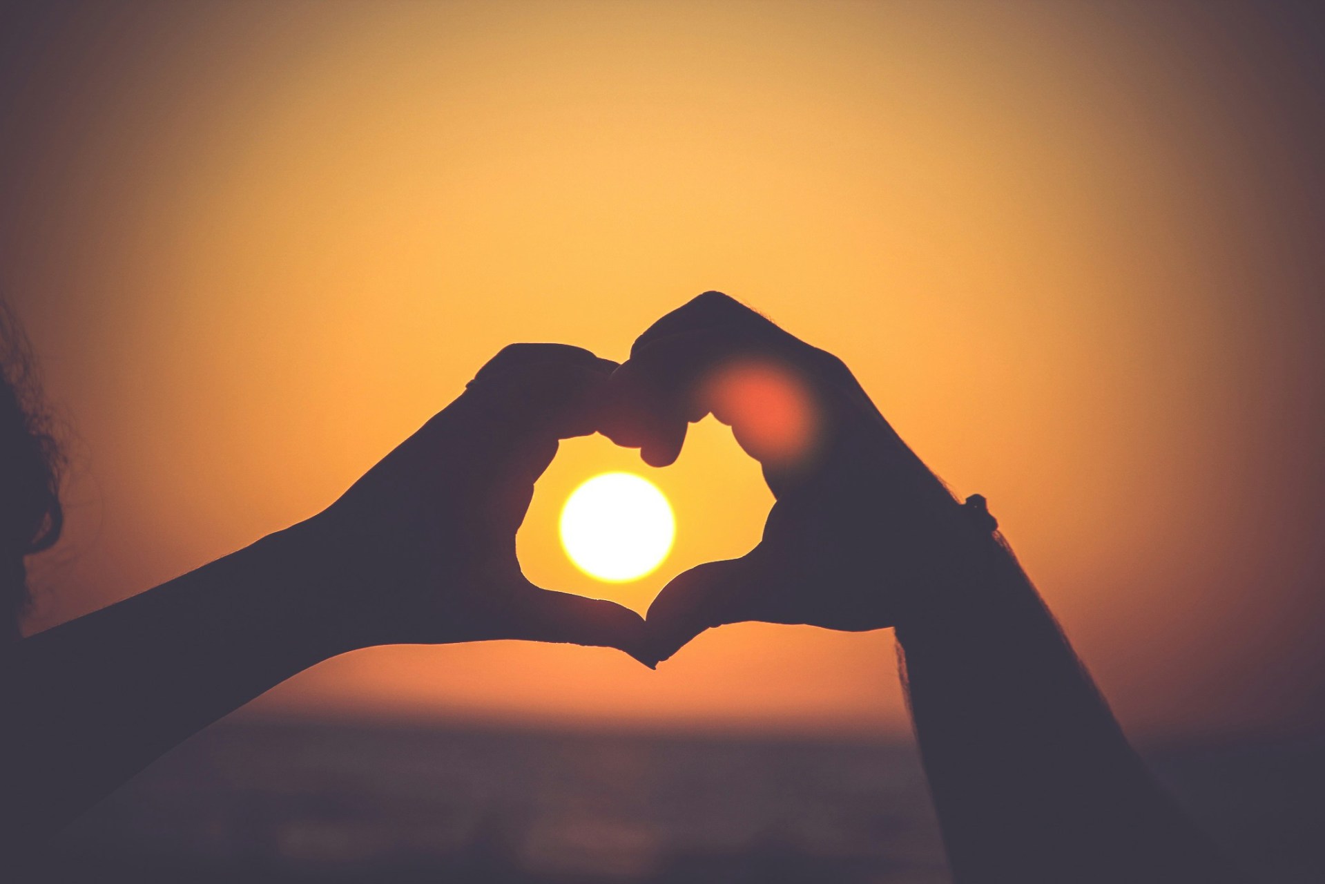 hands making a heart around a setting sun