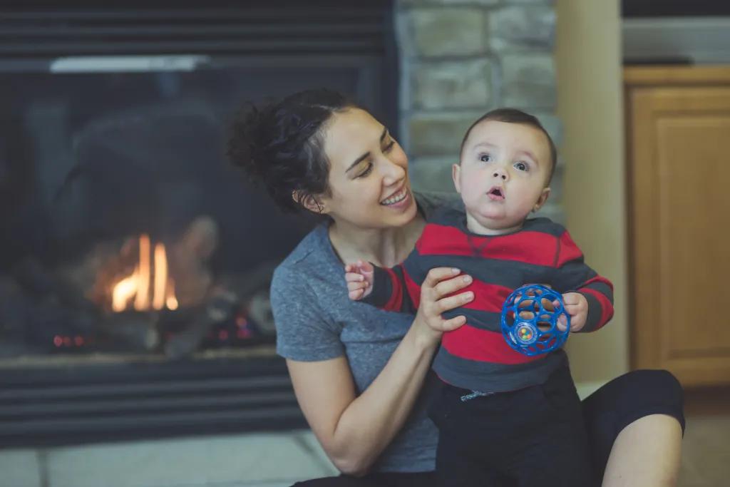 Mum holding son while sitting on the floor in front of a fireplace